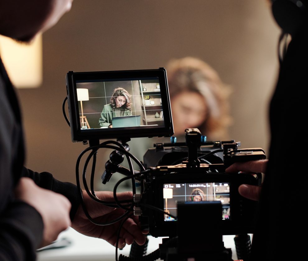 Close-up of steadicam screens with female model using laptop by table